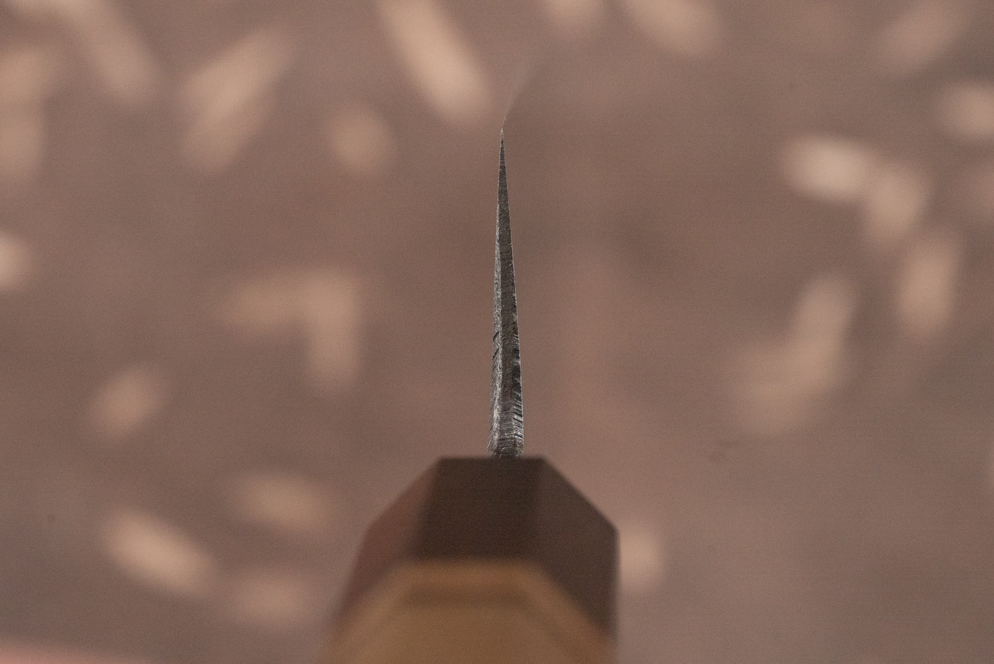 Close-up of Touroku Sakai Aogami Damascus Kiritsuke Petty 150mm knife blade, showcasing its sharp edge and tip, with handle faintly visible, reflecting exceptional Japanese craftsmanship ideal for precise cutting tasks.