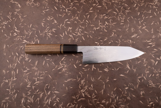 Touroku Sakai Aogami Damascus Kiritsuke Santoku 180mm knife with a laminated steel blade and kanji inscriptions, featuring an octagonal Wa-style handle of contrasting woods, displayed on a textured surface.