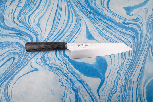 Touroku Sakai Gekka Bunka 180mm, a Japanese kitchen knife with a dark wooden handle and dimpled blade displaying Japanese characters, on a marbled surface, embodies exceptional craftsmanship and balance.