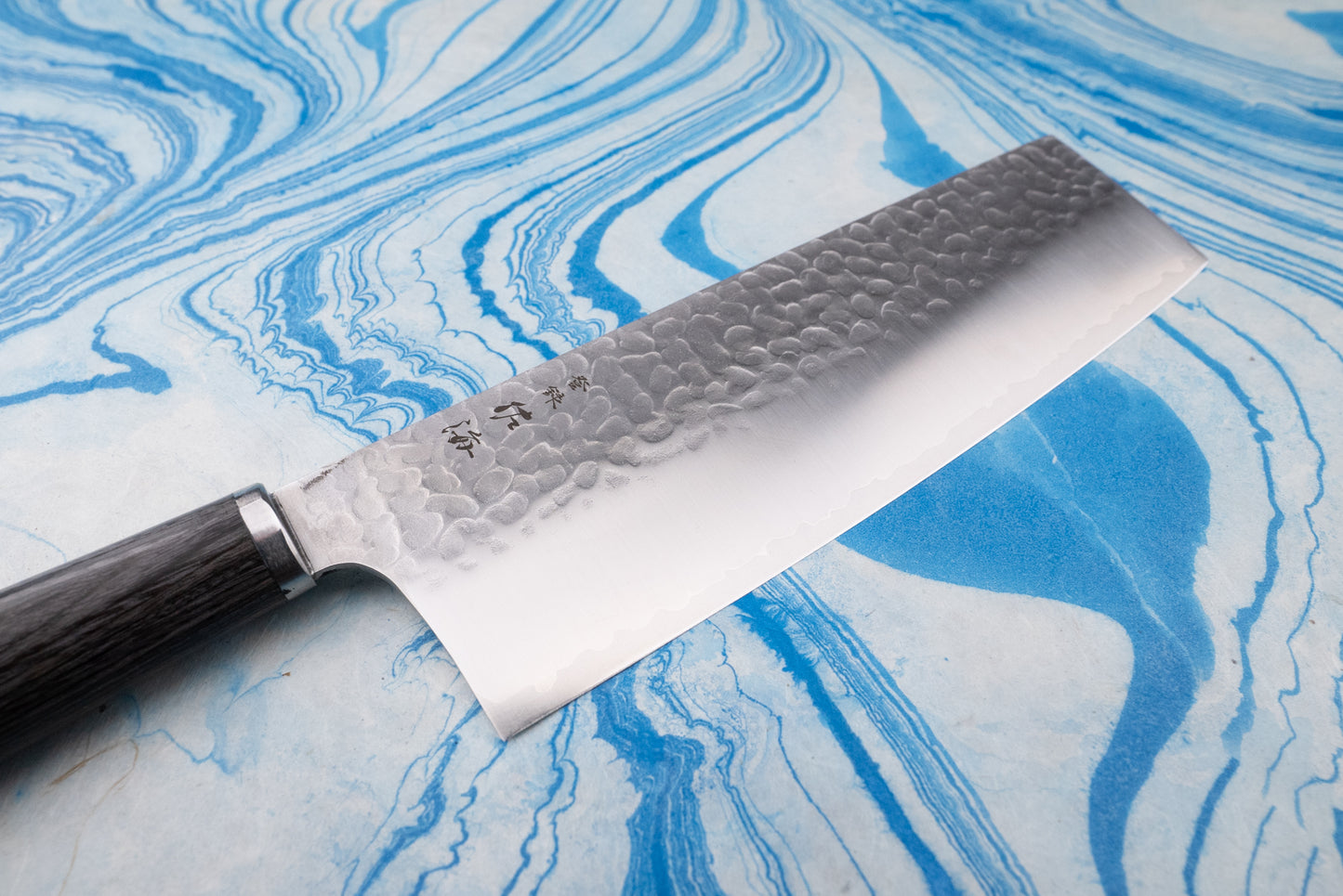 Touroku Sakai Gekka Nakiri 180mm knife with a hammered finish and stamped Japanese characters, featuring a wide, rectangular blade and dark wooden handle, resting on a marble-patterned surface.