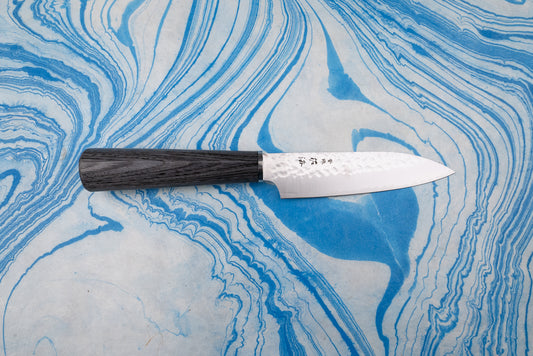 Touroku Sakai Gekka Petty 120mm knife with a hammered VG10 stainless steel blade and dark wooden handle, displayed on a marbled surface, showcasing fine Japanese craftsmanship and exceptional balance.