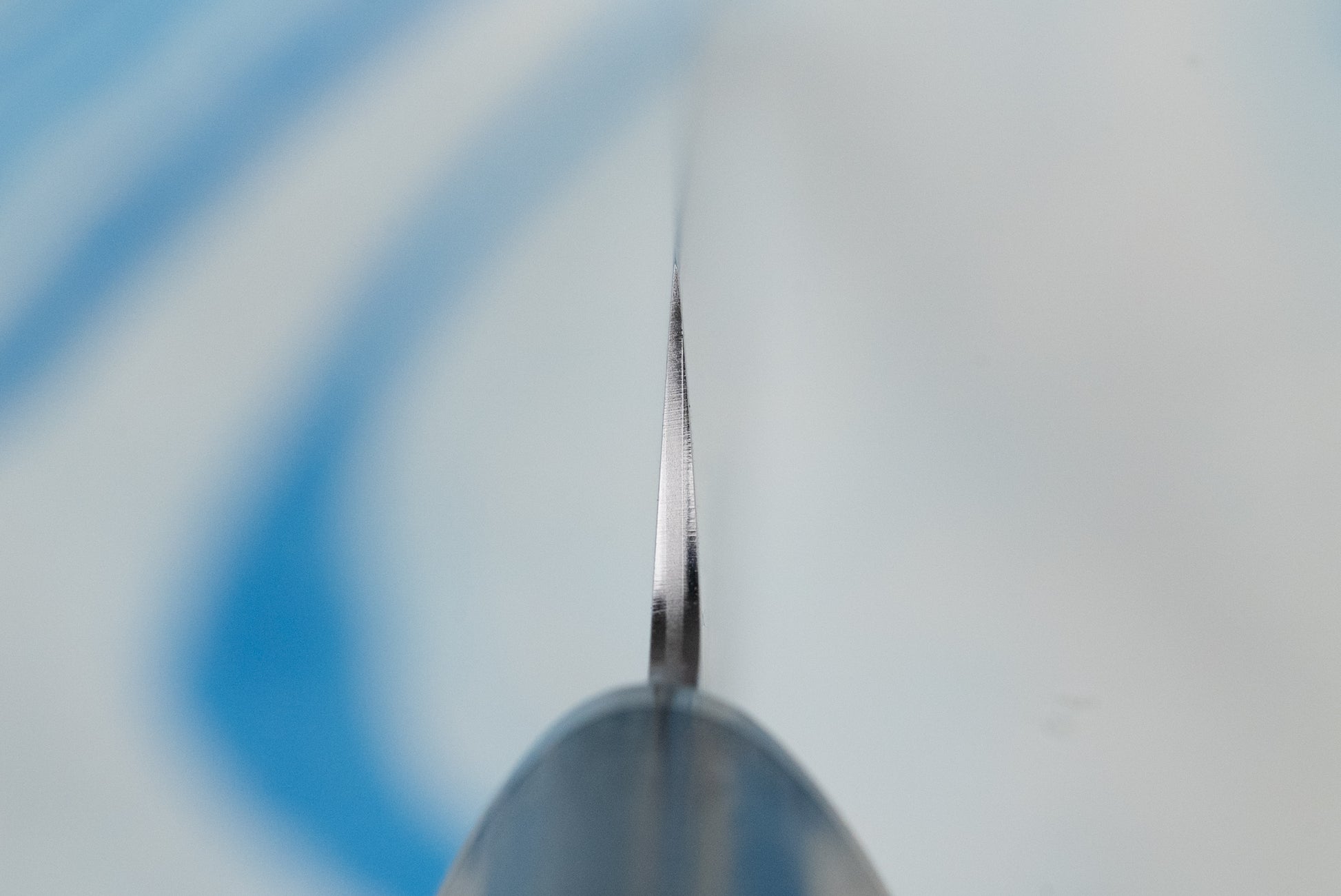 Touroku Sakai Gekka Petty 120mm knife, seen edge-on in a macro view, showcasing its razor-sharp VG10 stainless steel blade, ideal for precise cutting tasks on a board.