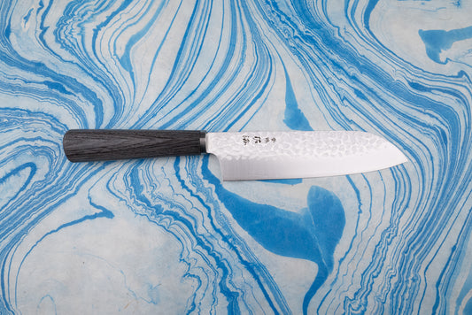 Touroku Sakai Gekka Santoku 170mm features a hammered Damascus-patterned blade with etched Japanese characters and a dark wooden handle, resting elegantly on a marbled surface.