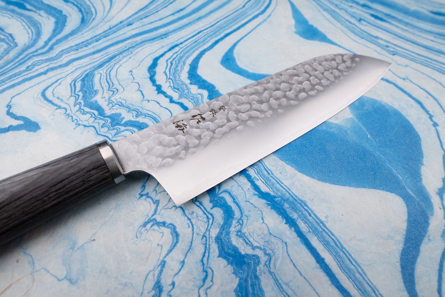 Touroku Sakai Gekka Santoku 170mm knife with a hammered stainless-steel blade, engraved Japanese characters, and a dark wooden handle, showcased on a marbled surface, epitomizing Japanese craftsmanship.