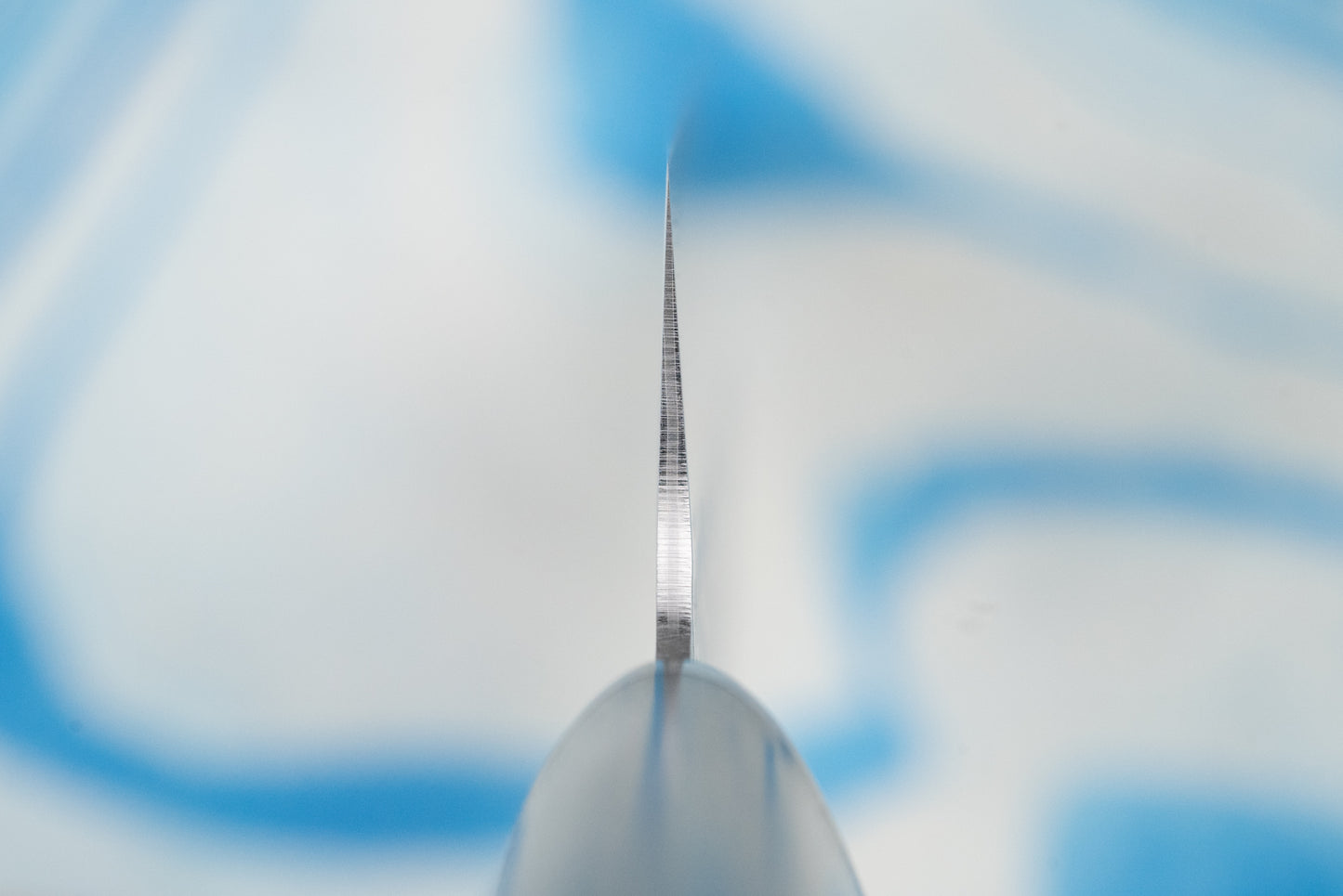 Close-up of the Touroku Sakai Gekka Santoku 170mm knife blade, showcasing its thin, finely ground spine tapering towards the tip, with the handle's butt subtly out-of-focus, emphasizing craftsmanship and balance.