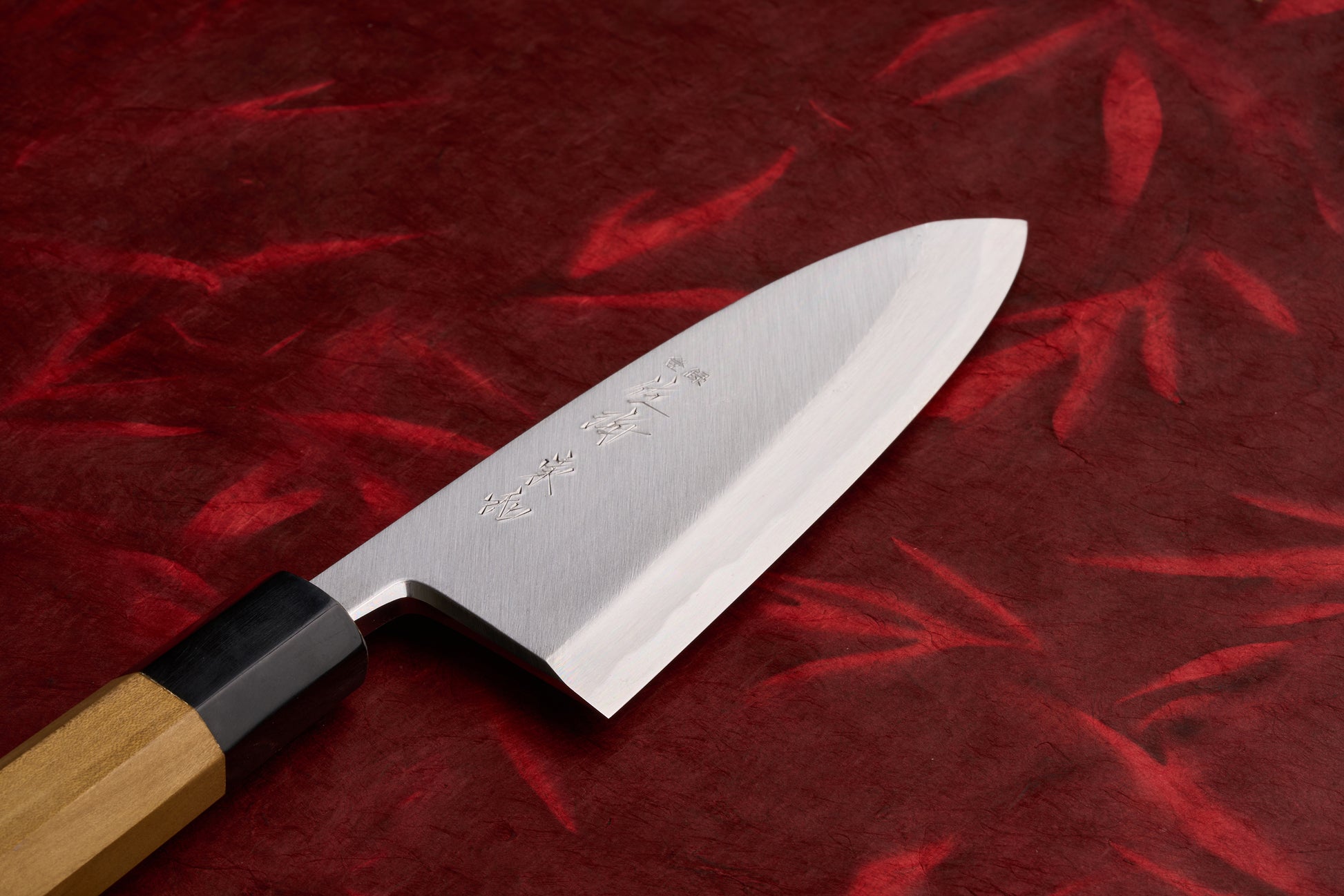 Touroku Sakai Tohwa Shirogami Deba 150mm, a traditional Japanese kitchen knife with a single-bevel stainless blade and kanji markings, rests on a red cloth, featuring an octagonal wooden handle.