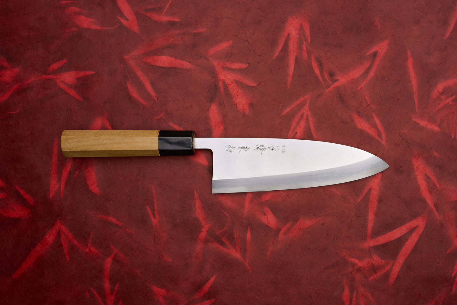 Touroku Sakai Tohwa Shirogami Deba 180mm, a Japanese kitchen knife with an engraved stainless steel blade and octagonal wooden handle, showcased on a red textured background.