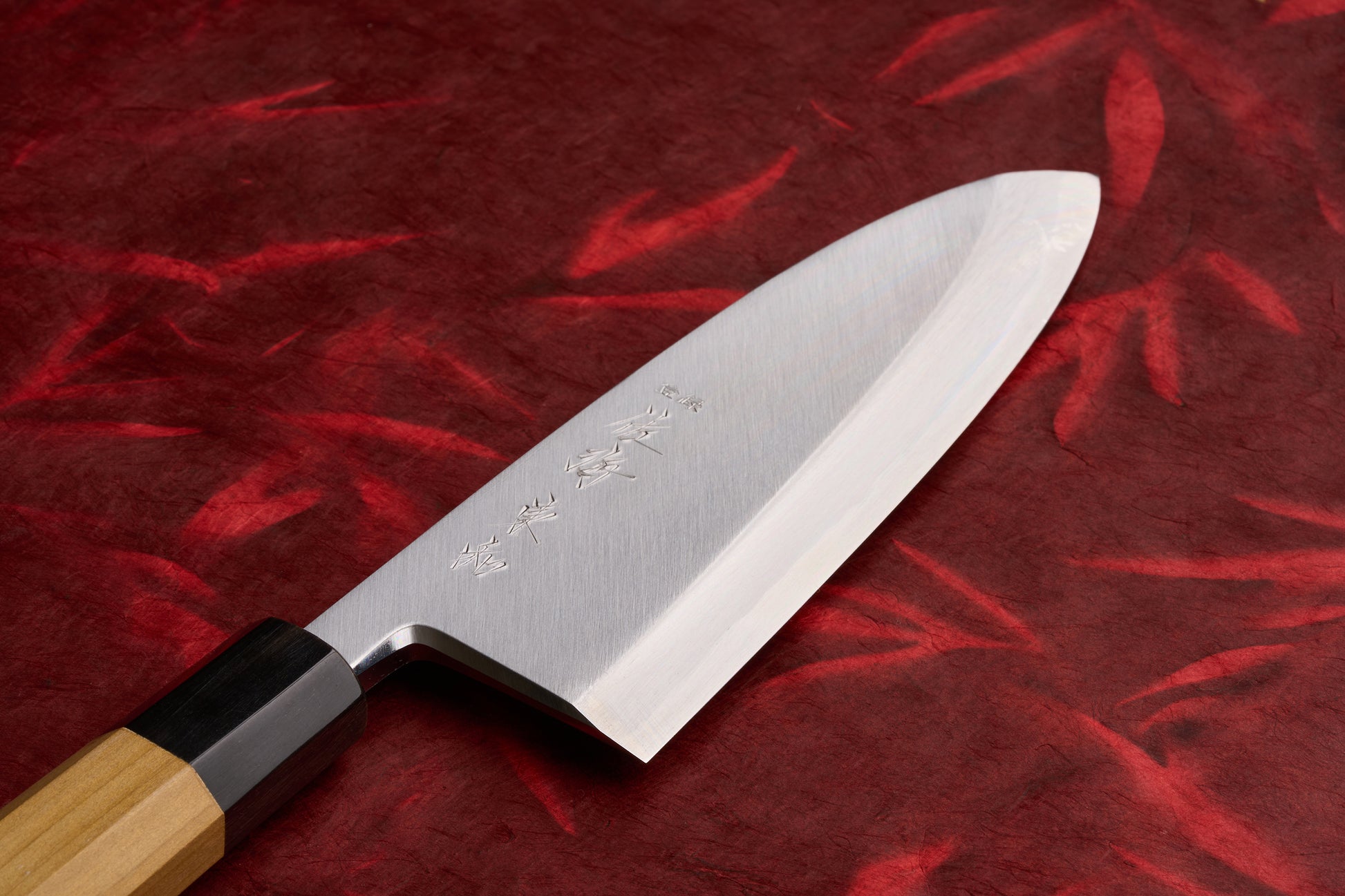 Touroku Sakai Tohwa Shirogami Deba 180mm knife with polished steel blade featuring kanji, octagonal wooden handle on red patterned cloth, exemplifying master sharpener Masaya Shimizu's craftsmanship.