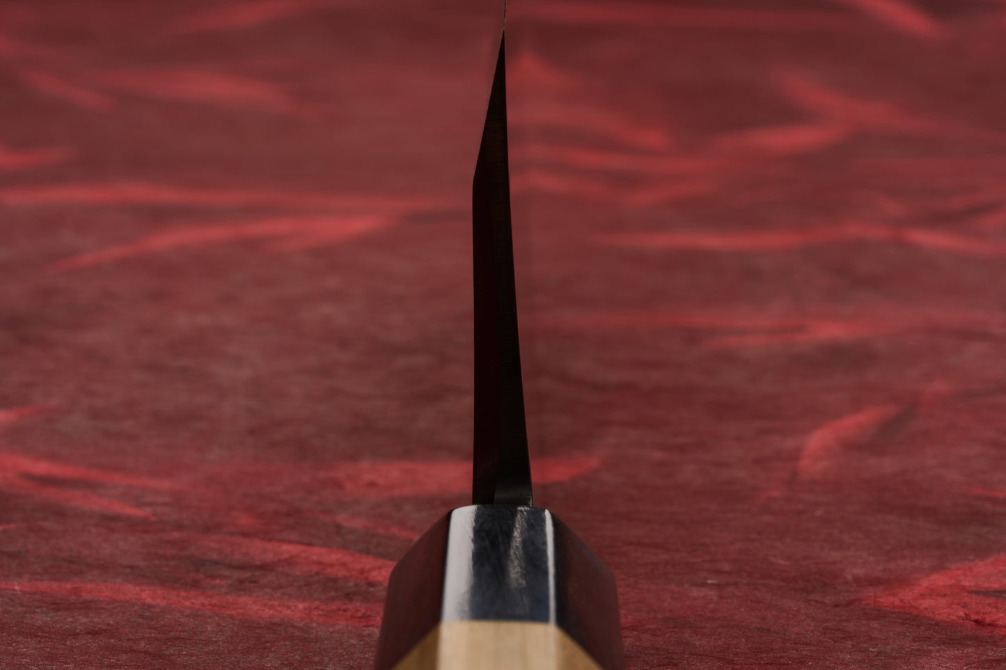 Touroku Sakai Tohwa Shirogami Deba 180mm stands upright, showcasing its elegant wood-metal handle and precise single bevel blade, set against a soft red fabric backdrop, embodying expert Japanese craftsmanship.