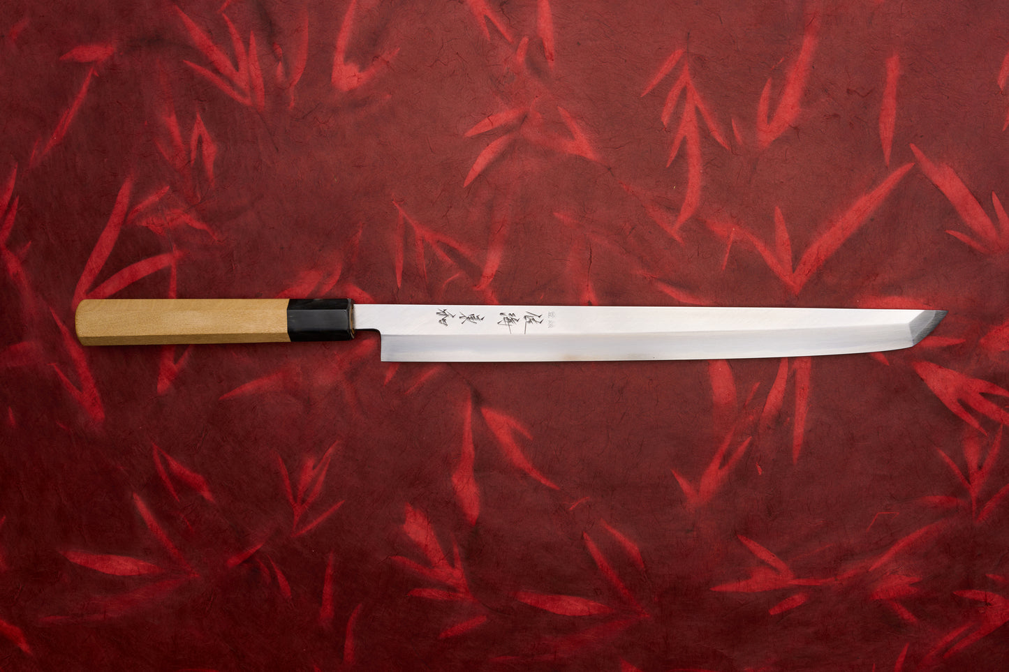 Touroku Sakai Tohwa Shirogami Sakimaru Takohiki 300mm knife, featuring a long, single-bevel blade with Japanese inscriptions and a light wooden handle, set against a bamboo-leaf–patterned background.
