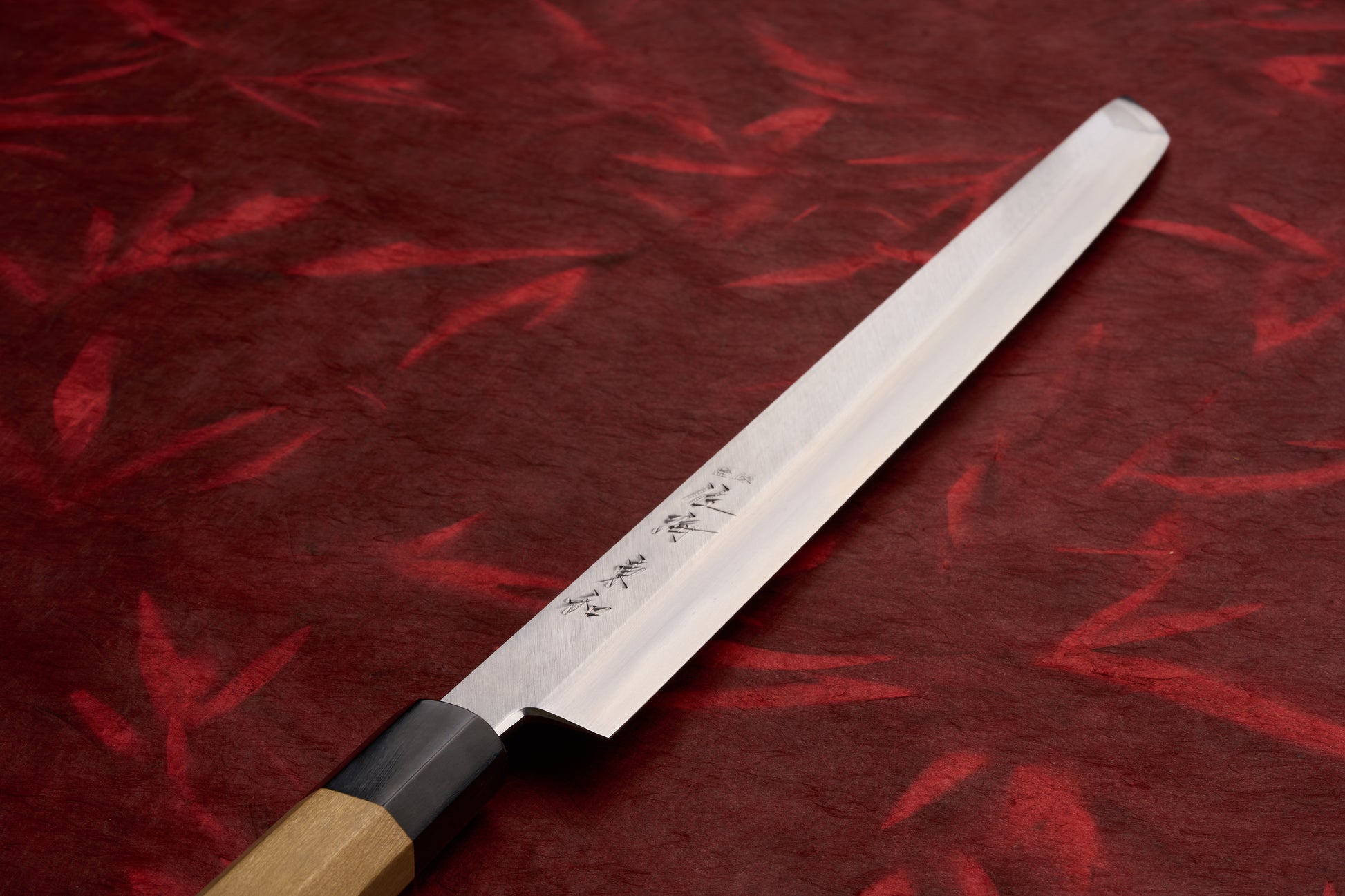Touroku Sakai Tohwa Shirogami Sakimaru Takohiki 300mm, a yanagiba knife with a single-bevel blade engraved with kanji, octagonal wooden handle, resting on a textured red surface.