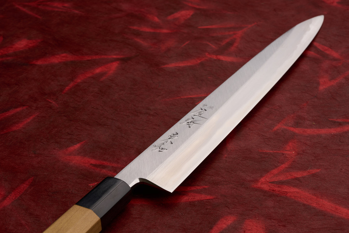 Touroku Sakai Tohwa Shirogami Yanagiba 270mm; a polished, single-edged knife with engraved kanji, octagonal wooden handle, ideal for slicing sashimi, showcasing Japanese craftsmanship on a deep-red textured surface.