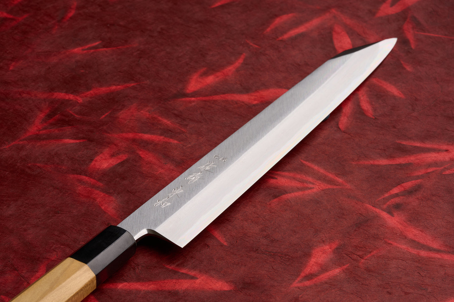 Touroku Sakai Tohwa Shirogami Kiritsuke Yanagiba 270mm knife with engraved kanji on polished steel blade and octagonal wooden handle, showcased on a red textured cloth, highlighting its craftsmanship.