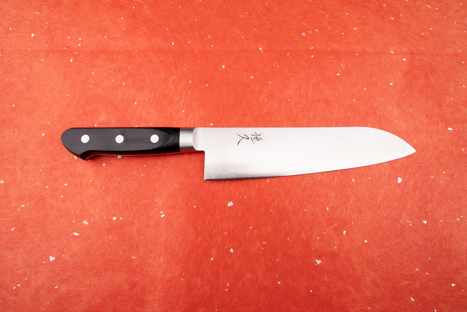 Tsunehisa 440C Sanjuni 参拾弐 Western Santoku 180mm T-03205: A Japanese-style chef's knife with a sleek steel blade, wavy temper line, and black triple-riveted handle, featured against a textured backdrop.