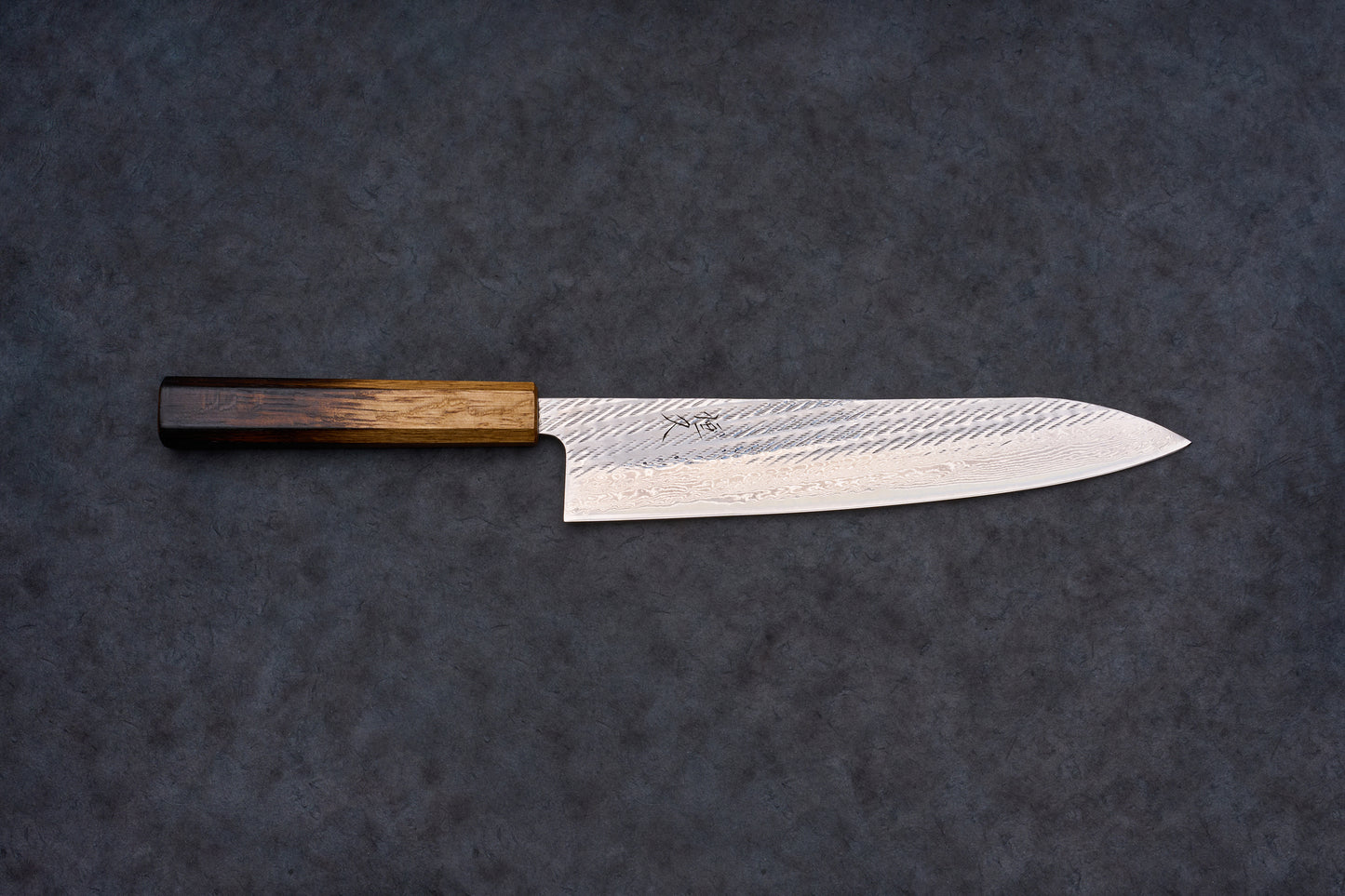 Tsunehisa AUS10 Sanjushichi Nawame Damascus Gyuto 240mm features a Damascus-patterned blade with a maker's mark and an octagonal wooden handle, laid on a textured surface.