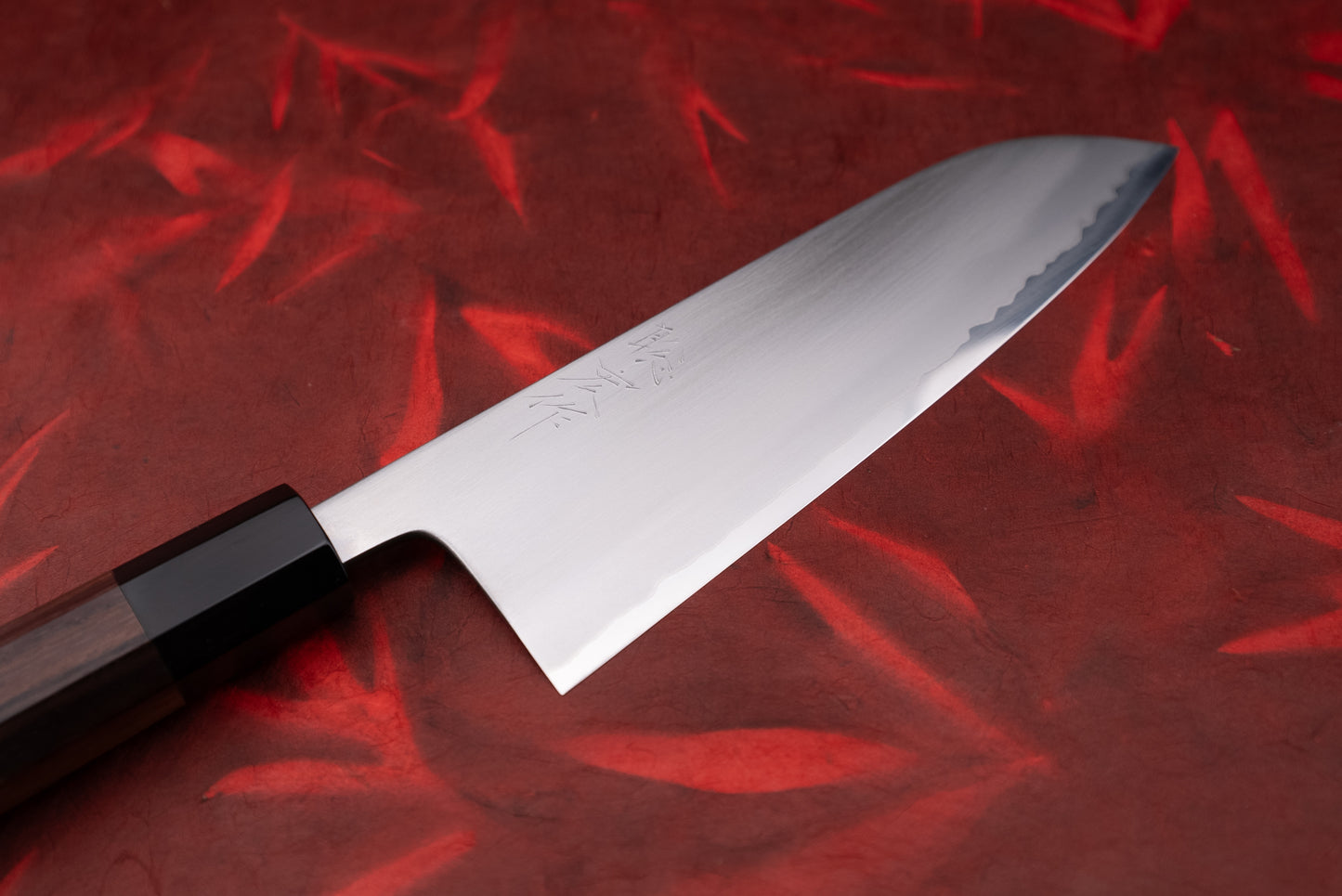Toshihiro Wakui Shirogami Stainless Migaki Santoku 180mm on a textured surface, showcasing its single-bevel blade with hamon pattern and octagonal rosewood handle, embodying Japanese craftsmanship.