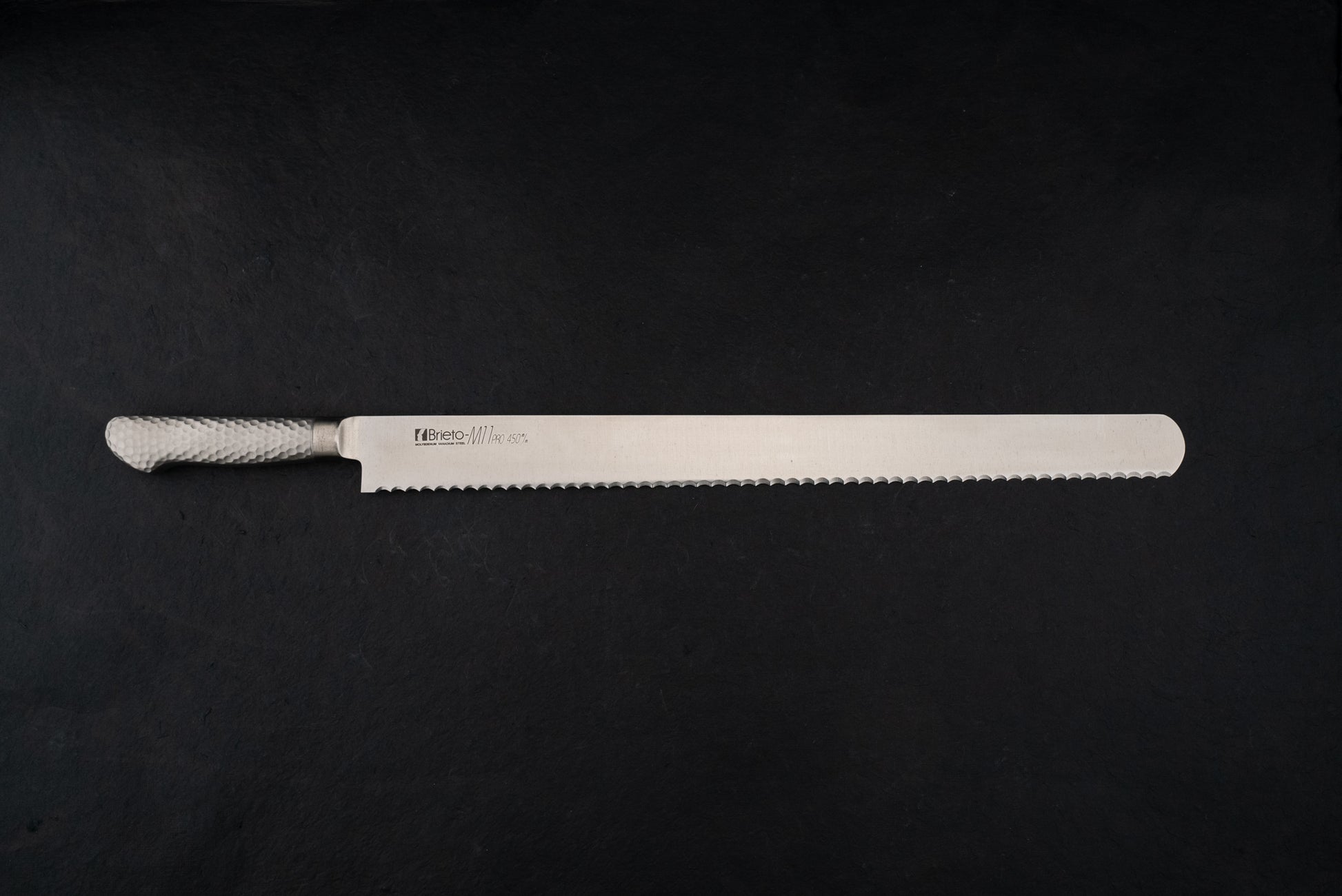 Brieto Pro Bread Knife 450mm M1146 with a hammered metal handle and extra-long serrated blade, ideal for precise slicing, showcased against a dark backdrop, embodying Knifewear's dedication to unique Japanese craftsmanship.