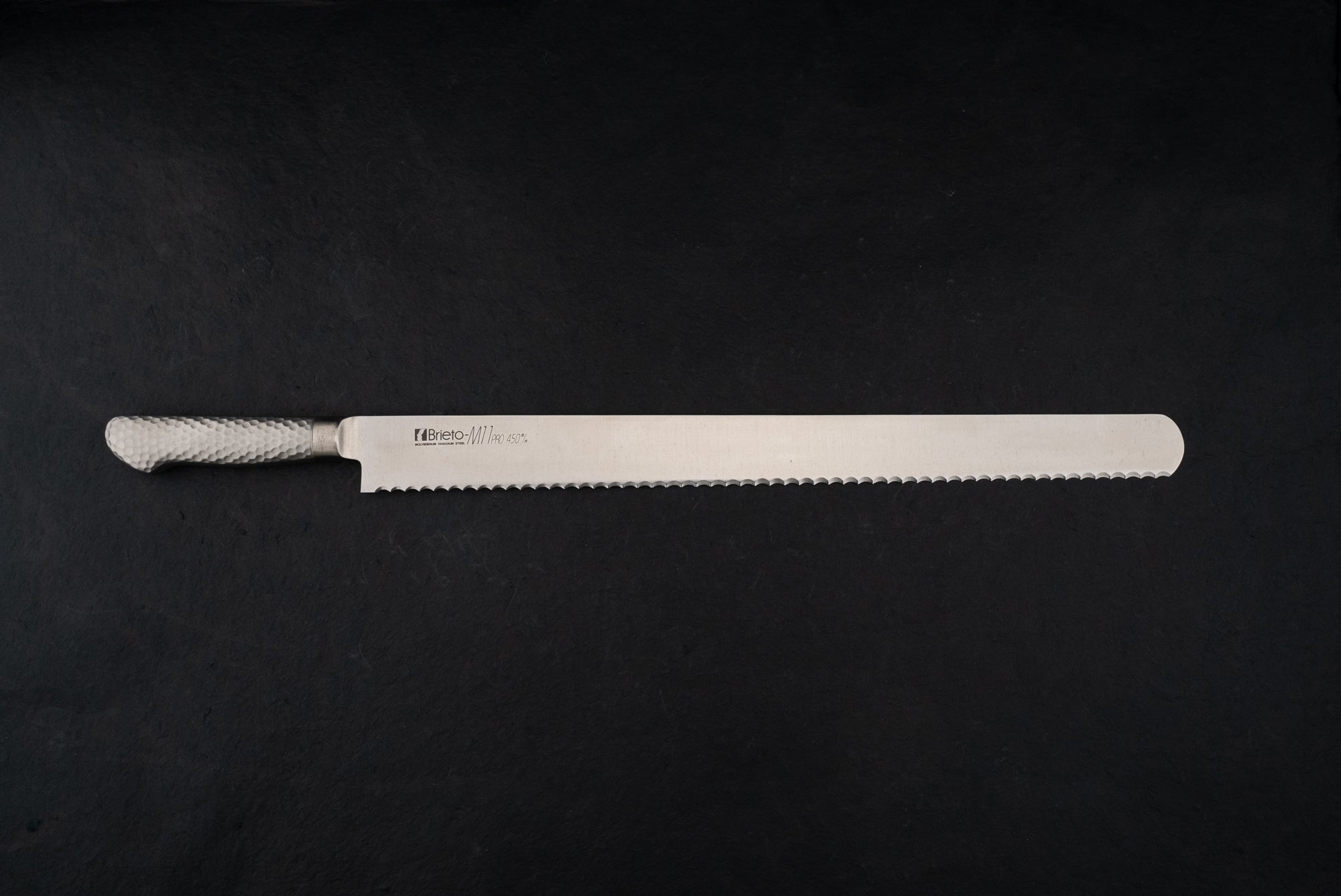 Brieto Pro Bread Knife 450mm M1146 with a hammered metal handle and extra-long serrated blade, ideal for precise slicing, showcased against a dark backdrop, embodying Knifewear's dedication to unique Japanese craftsmanship.