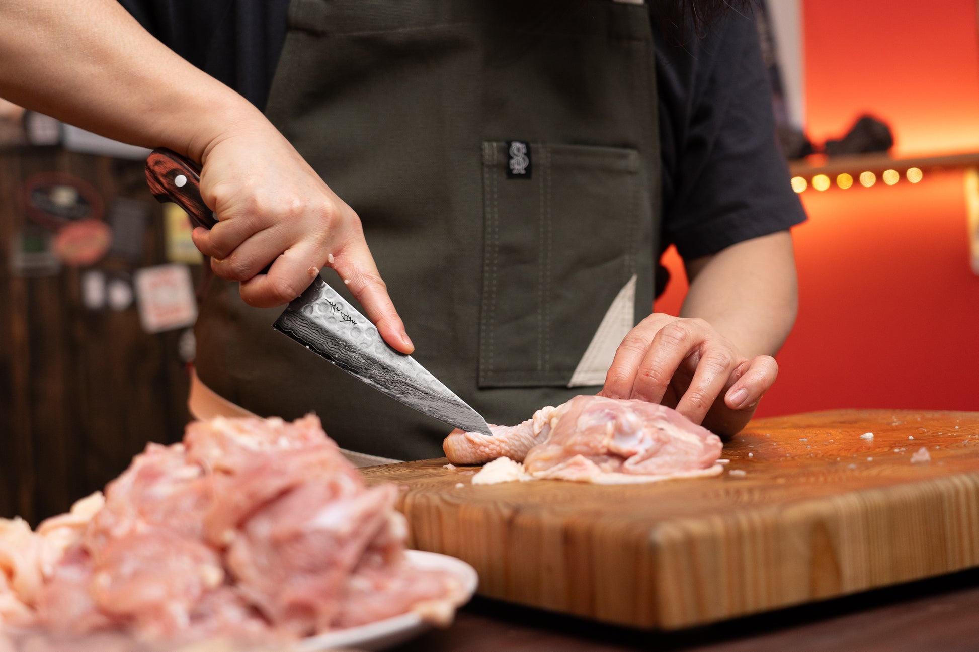 Yakitori Butchery & Skewering Class - Ottawa: A person cuts raw chicken on a wooden board, preparing for traditional Japanese yakitori skewering, reflecting Knifewear’s dedication to culinary craftsmanship.