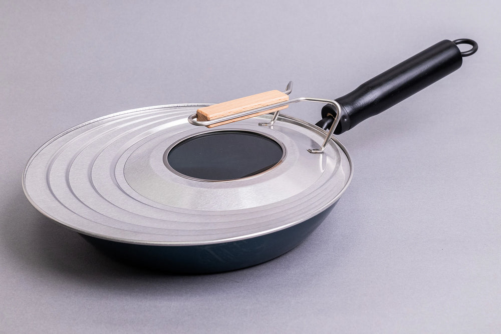 Fujita Kinzoku Stainless Steel Universal Lid, featuring a concentric-ridged design with a central glass window and wooden handle, securely fits pans for seamless cooking. Ideal for Japanese kitchen enthusiasts.