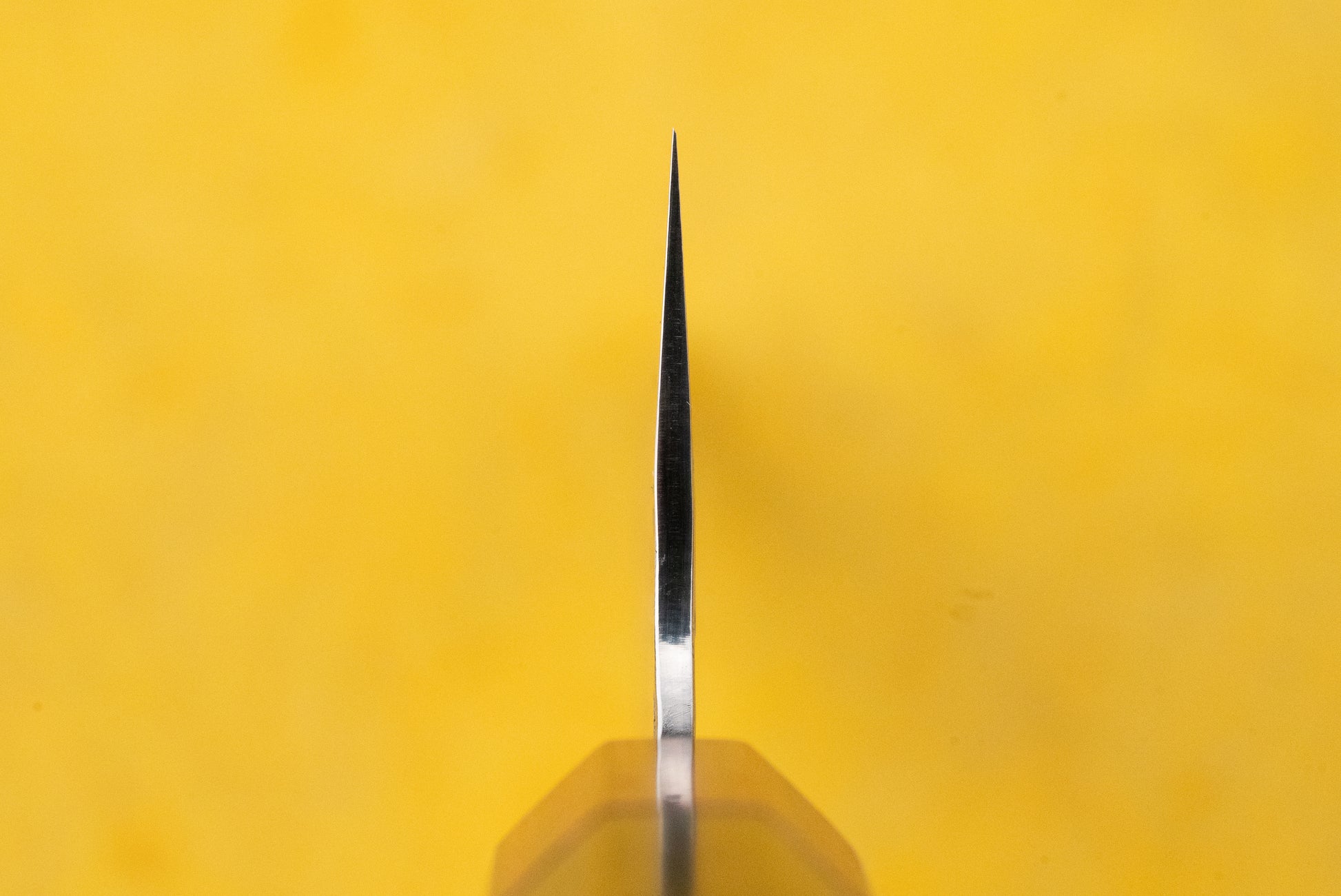Makoto Kurosaki Coreless Kaen Tsuchime Santoku 165mm, a precision-crafted chef’s knife with a thin blade edge, designed for slicing, dicing, and mincing, showcased vertically against a yellow background.